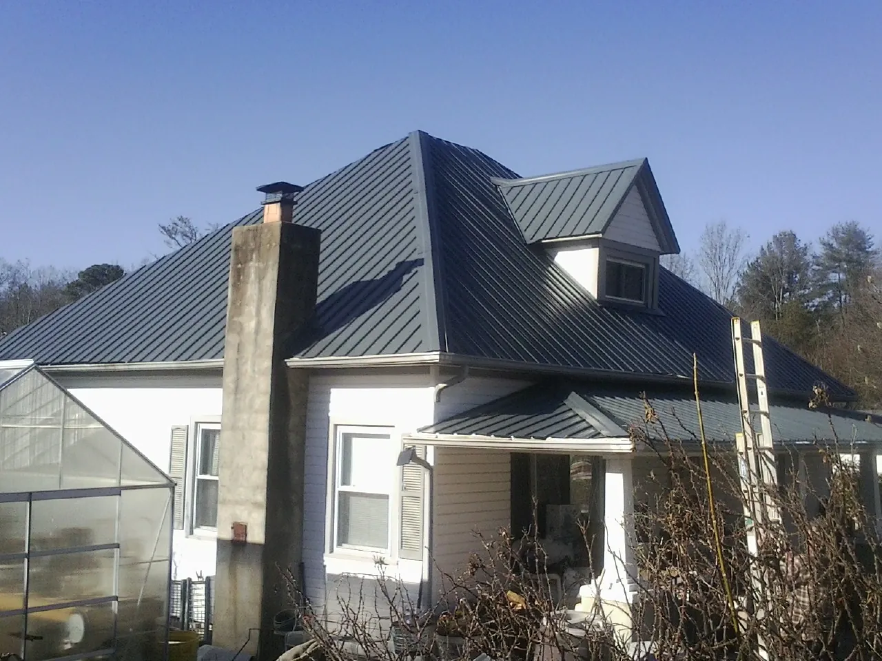 Dark blue standing seam metal roof on a white farmhouse with dormer — Slate & Tile Roof Repair by Roofing Brothers in Boulder Creek