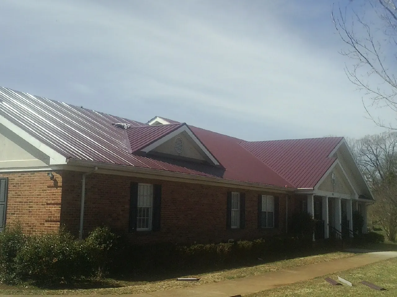 Red metal roof with gabled entries on a long brick building, from a Hail Damage Roof Repair job in Boulder Creek
