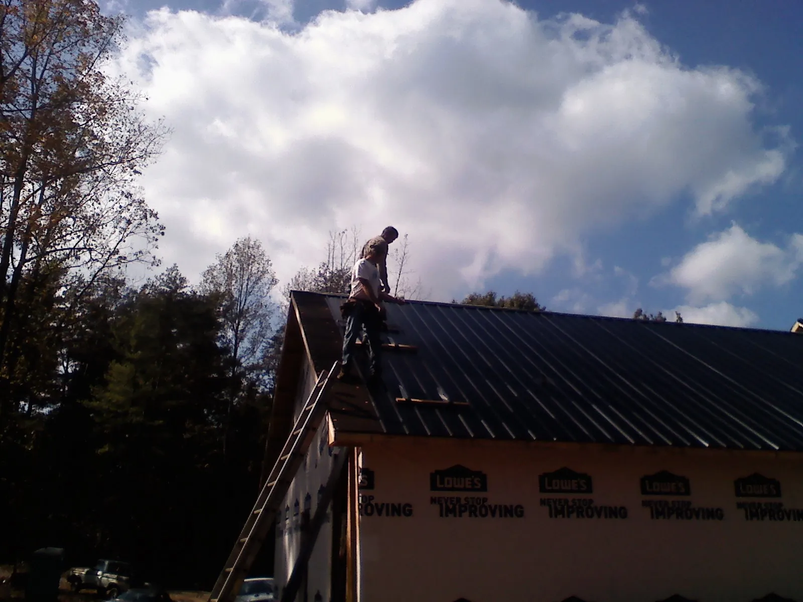 Roofer fastening dark metal panels high against a cloudy sky, from a Roof Inspection job in Boulder Creek