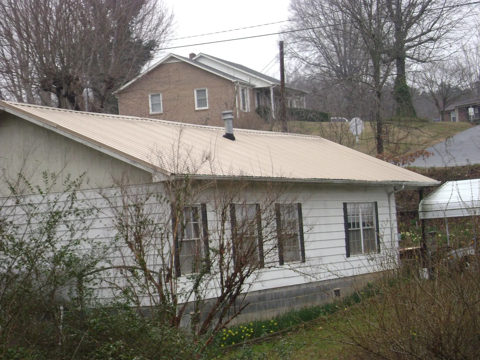 Tan metal roof on a white sided house set into a hillside — Commercial Roofing by Roofing Brothers in Boulder Creek